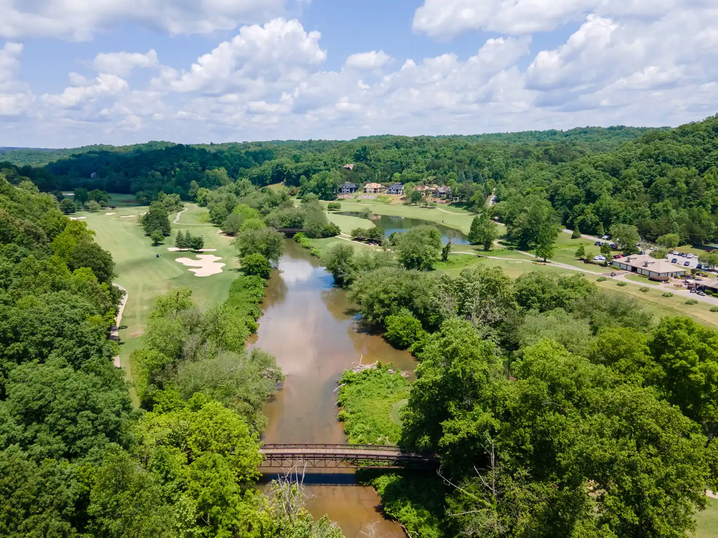 Aerial view of a river running between wooded banks with a pedestrian footbridge